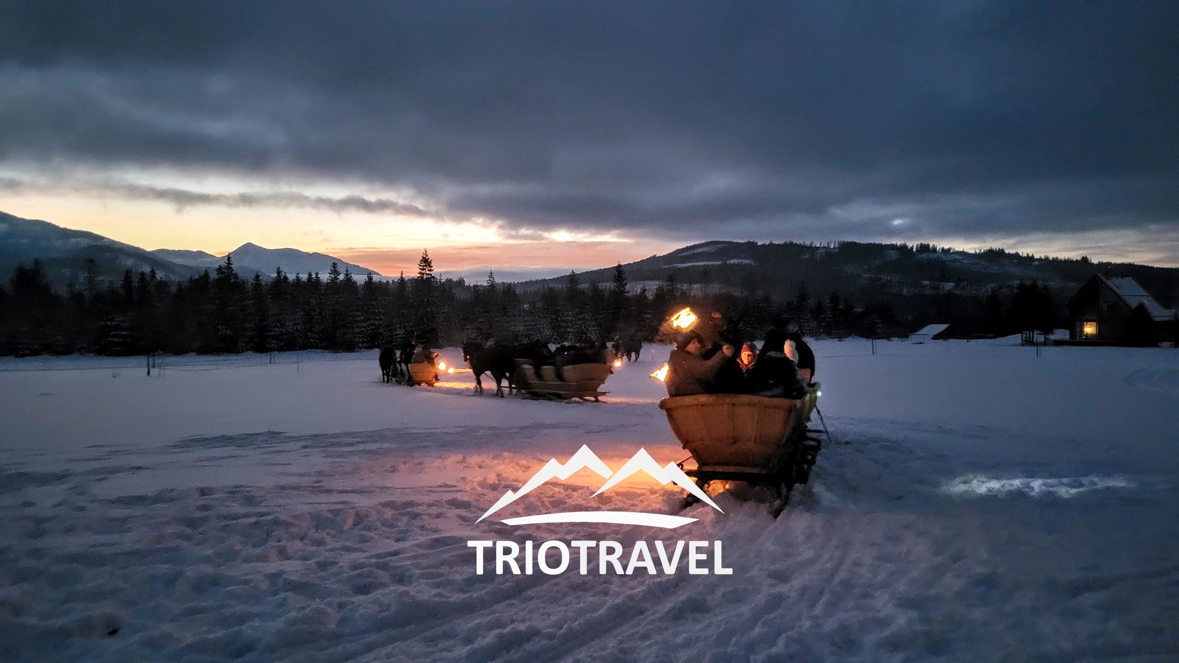 Uczestnicy kuligu z pochodniami w górskiej scenerii,