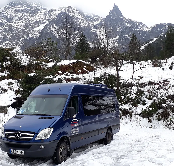 Navy blue bus against a backdrop of snow-covered mountains