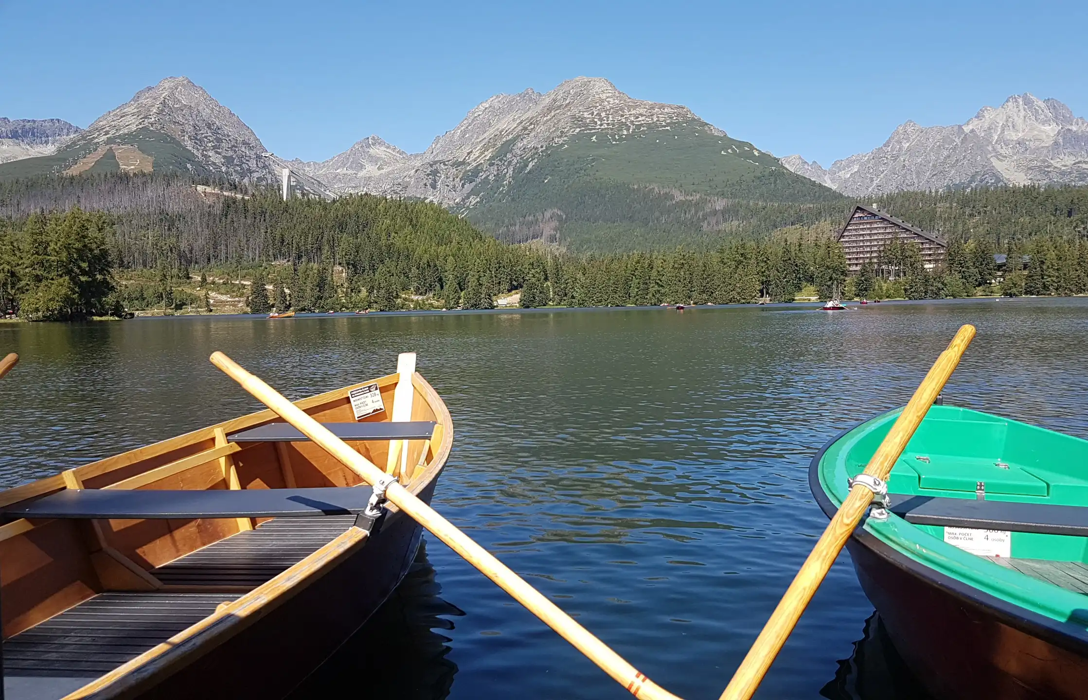 Two rowboats on Štrbské Pleso Lake, with a view of the High Tatras and the Patria Hotel in the background.