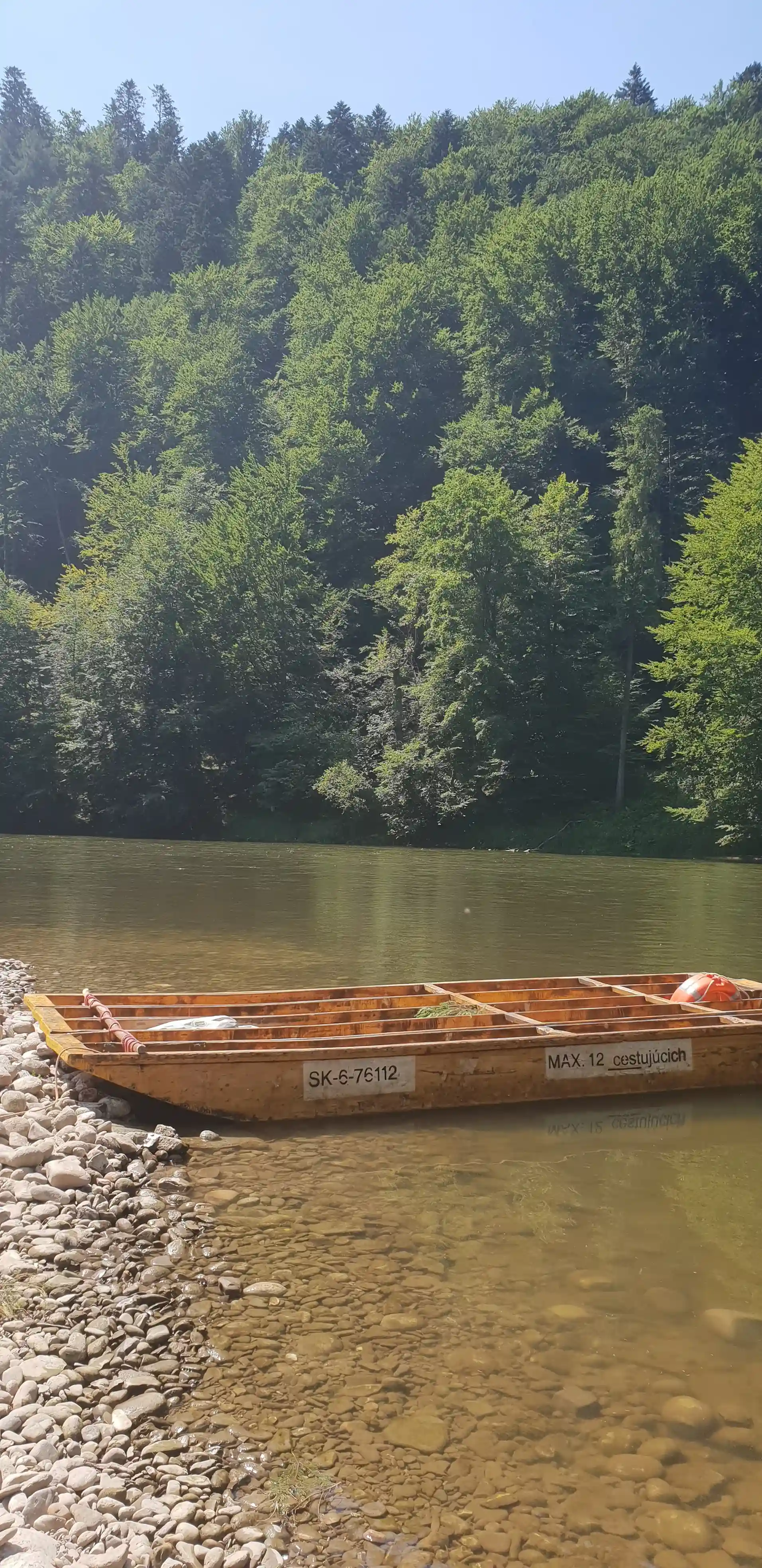 A boat floating on a river surrounded by trees and mountains, representing outdoor activity and transportation on water.