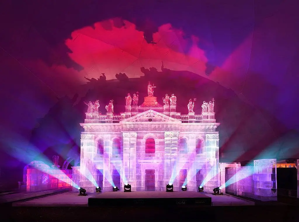 Fasada bazyliki wyrzeźbiona w lodzie, artystycznie oświetlona fioletowym i różowym światłem podczas wystawy Tatry Ice Master.