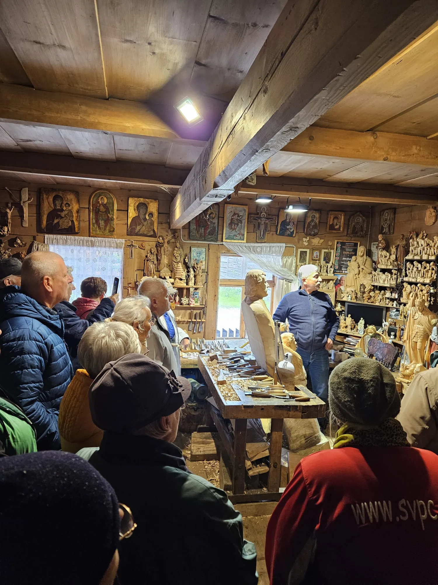 A group of people gathered in a room full of statues, presenting various works of art. The indoor scene emphasizes the ceiling above and the variety of clothing worn by those present.
